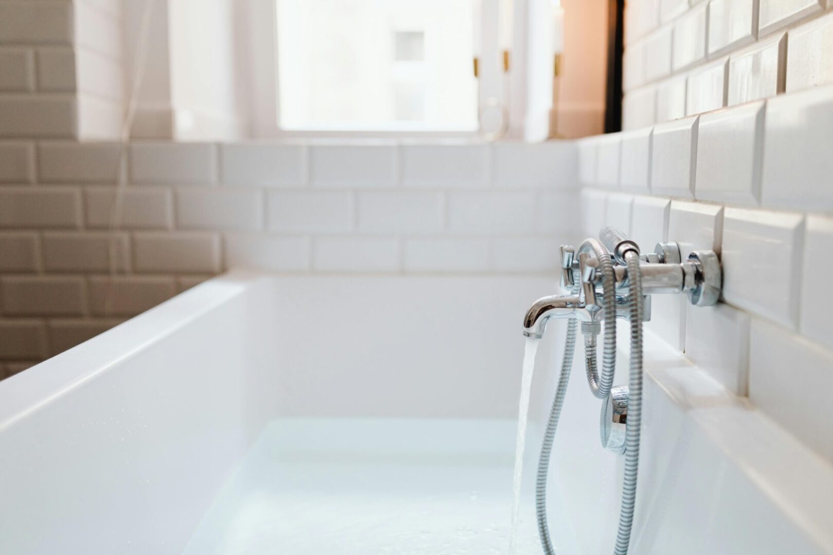 A white bathtub with a chrome faucet and tile walls.