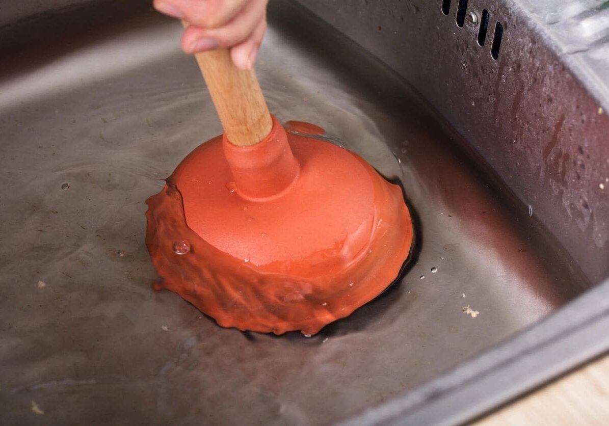 A person is using an orange plunger to clean the sink.