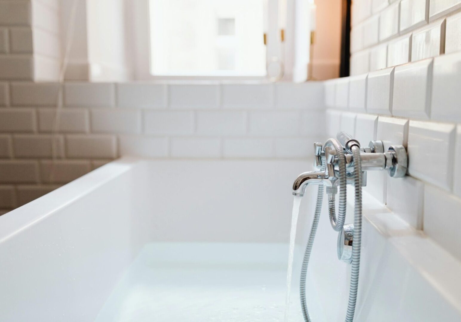 A white bathtub with a chrome faucet and tile walls.