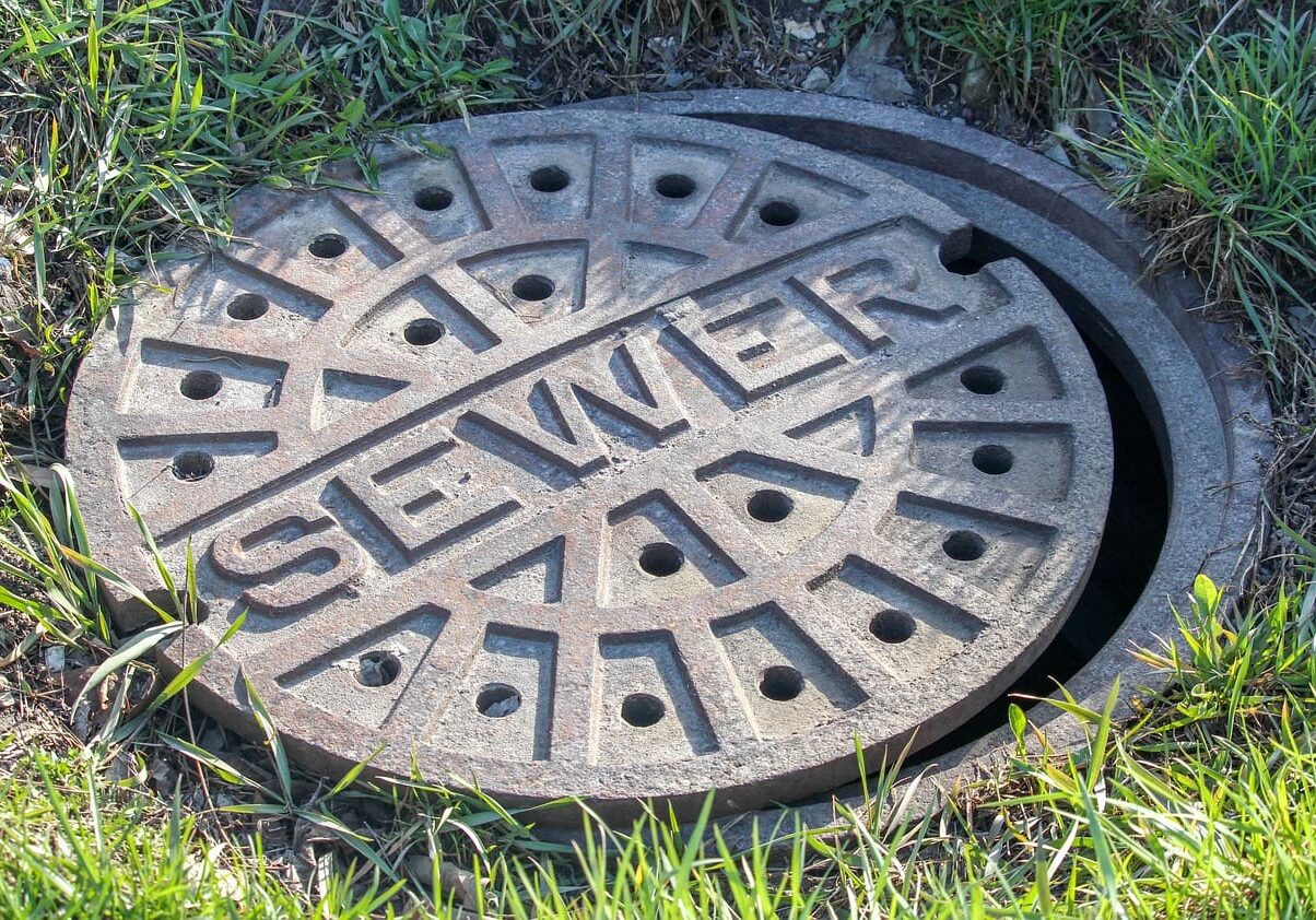 A sewer cover is shown in the grass.